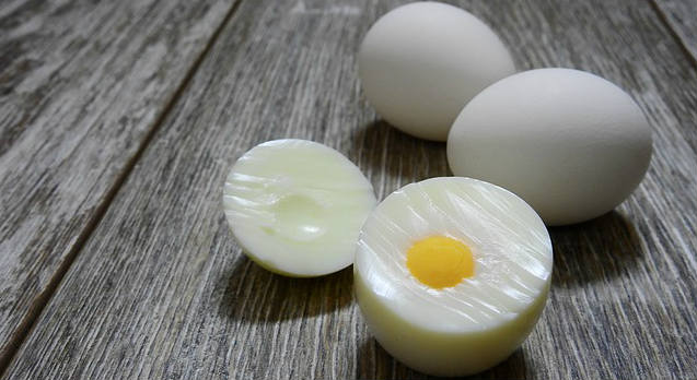 Whole and sliced hard boiled eggs without the shell resting on top of wood