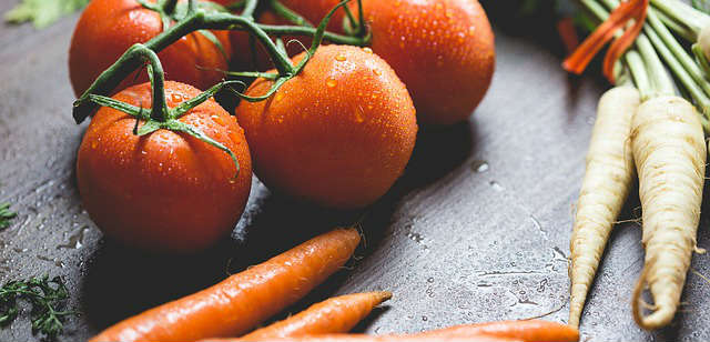 Washed raw tomatoes, carrots and parsnips sitting on tip of a wooden surface