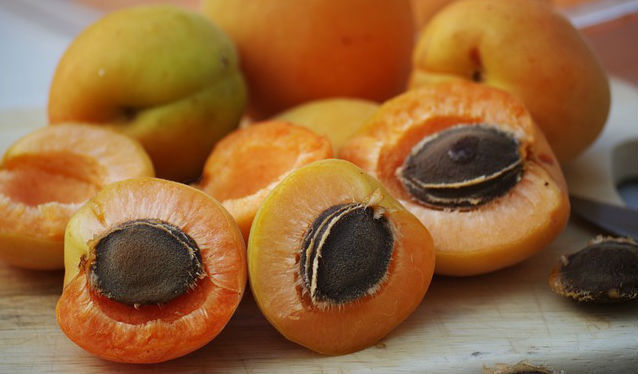 Whole and sliced apricots with their pits resting on top of a wooden table