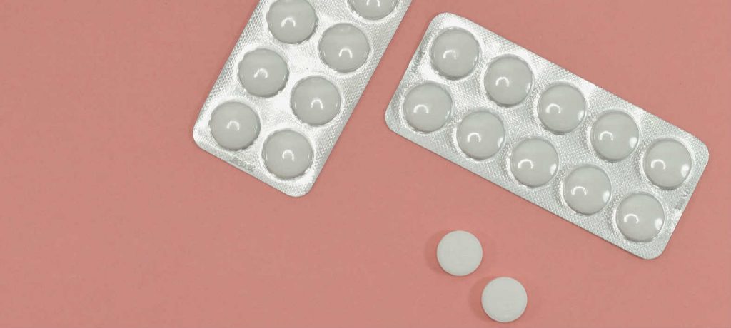 Two packets of white medication tablets overtop a pink background