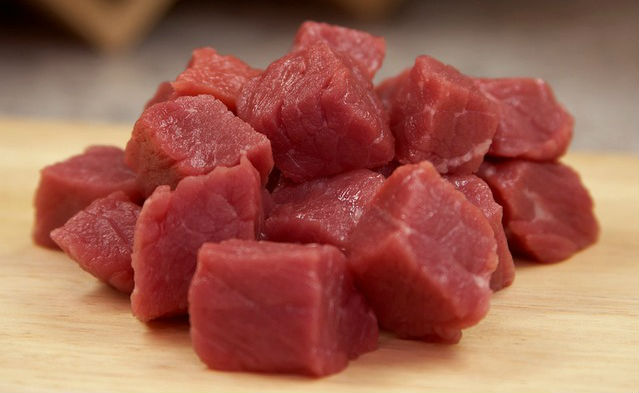 Cubed raw beef on a wooden cutting board