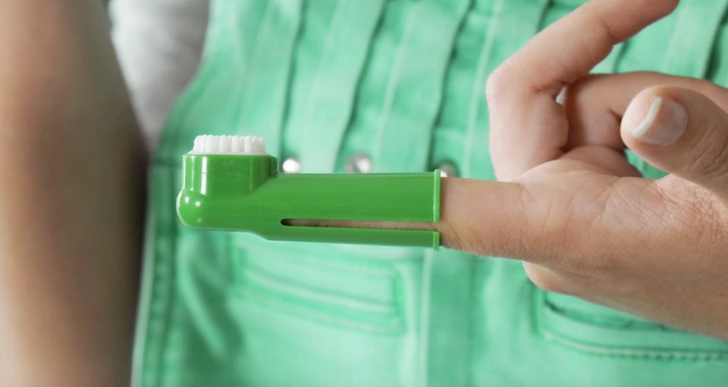 A woman has a green finger toothbrush inserted on her index finger