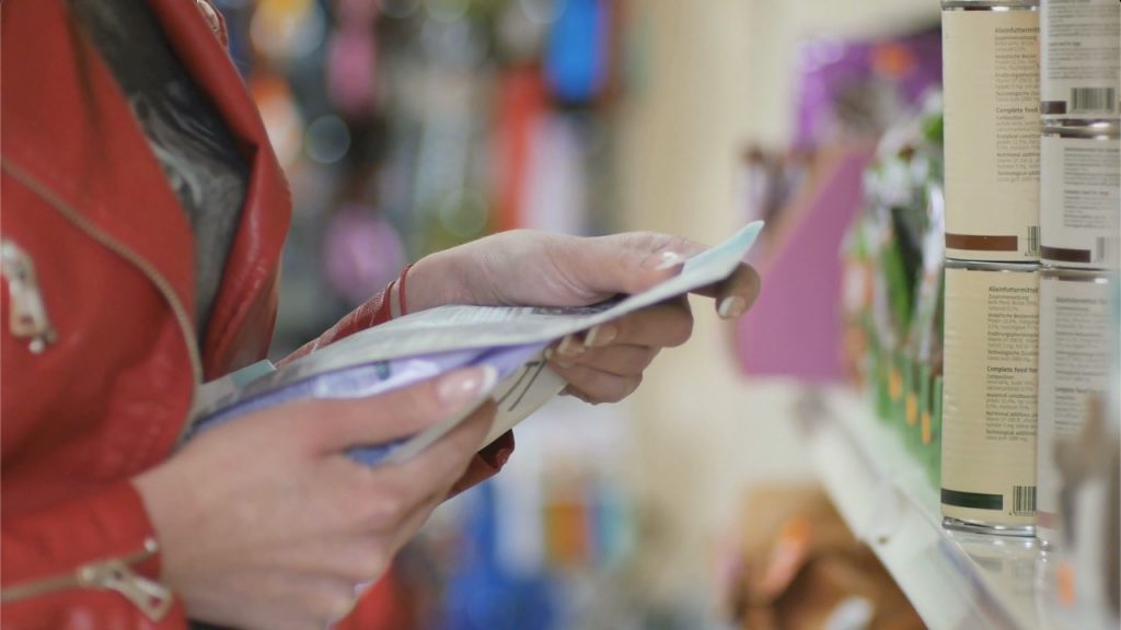 A woman is holding a bag of pet food and looking at the ingredients on the back in a pet store