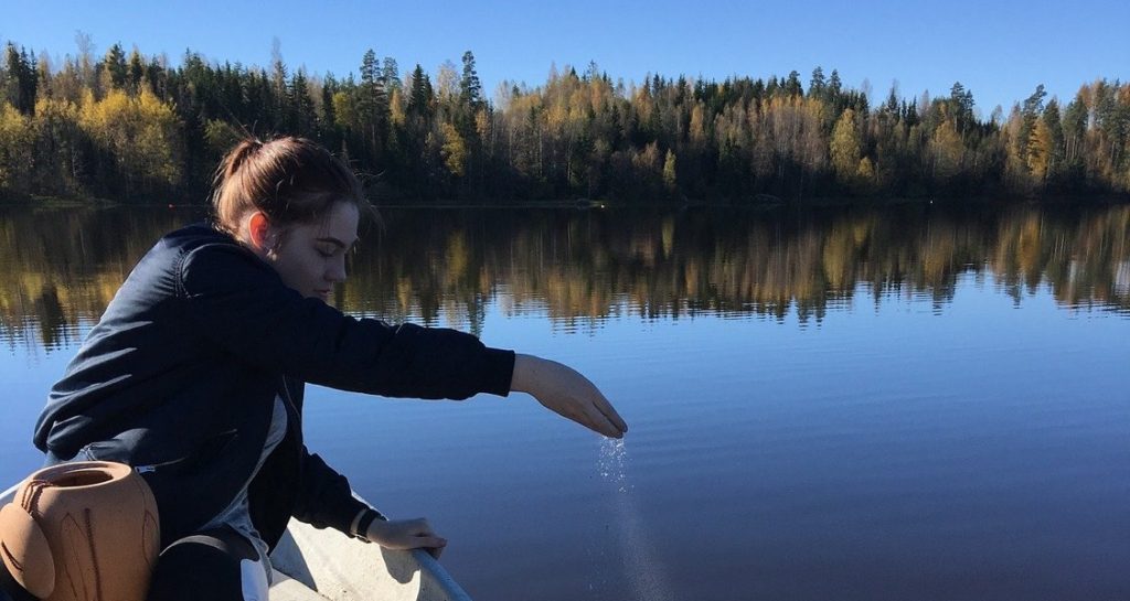 A woman is sitting on a boat and scattering cremation ashes on a lake