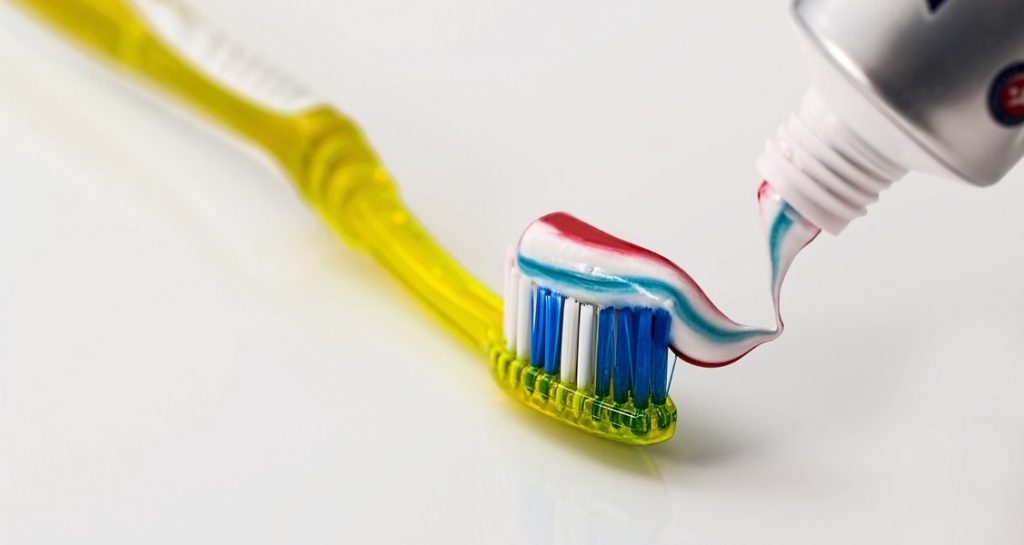 A multicolored toothpaste intended for humans is being spread on a yellow toothbrush