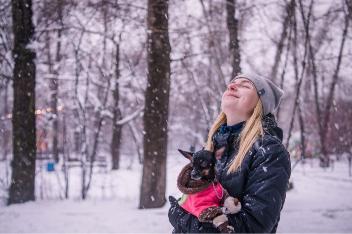 A young woman is holding a small dog wearing a pink winter jacket