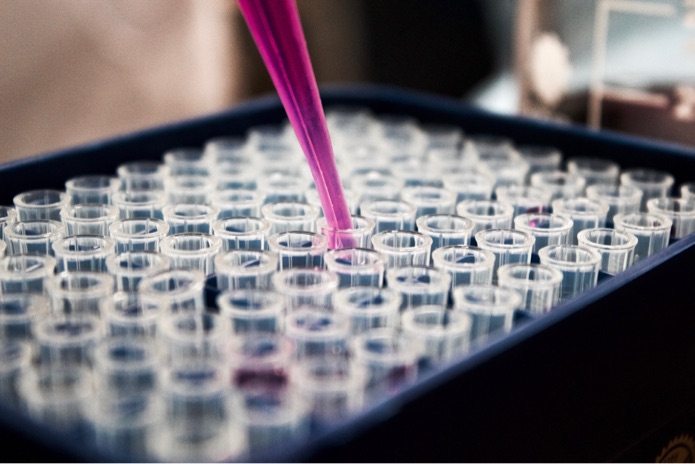 A pink pipette is dispensing a solution into a receptacle