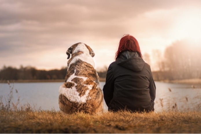 A woman and dog are sitting beside each other facing a body of water