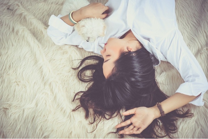 A girl is lying in bed with a small white dog in her arms