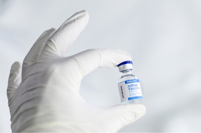 A person wearing white gloves holds a vial containing an mRNA Covid-19 vaccine