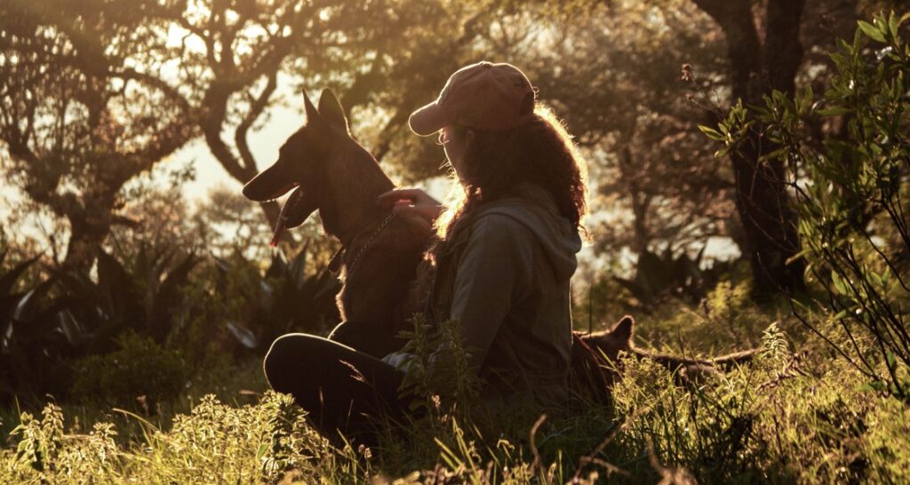 A woman is sitting in the woods with her dog