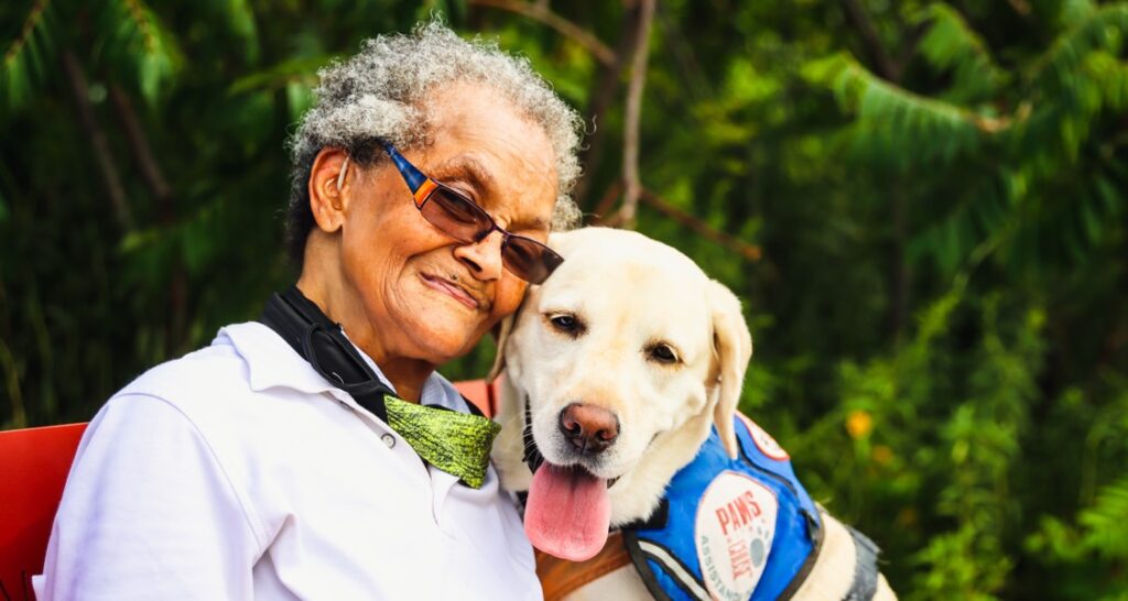 An elderly woman is sitting beside a dog outside