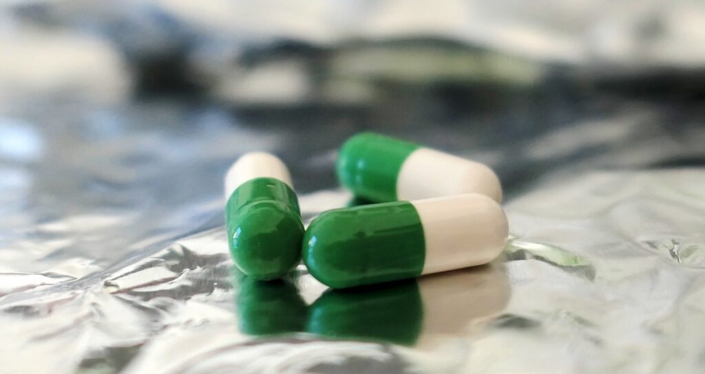 Green and white colored medication capsules situated on aluminium foil