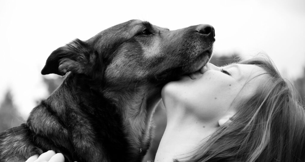 A woman is kissing a dog underneath their mouth