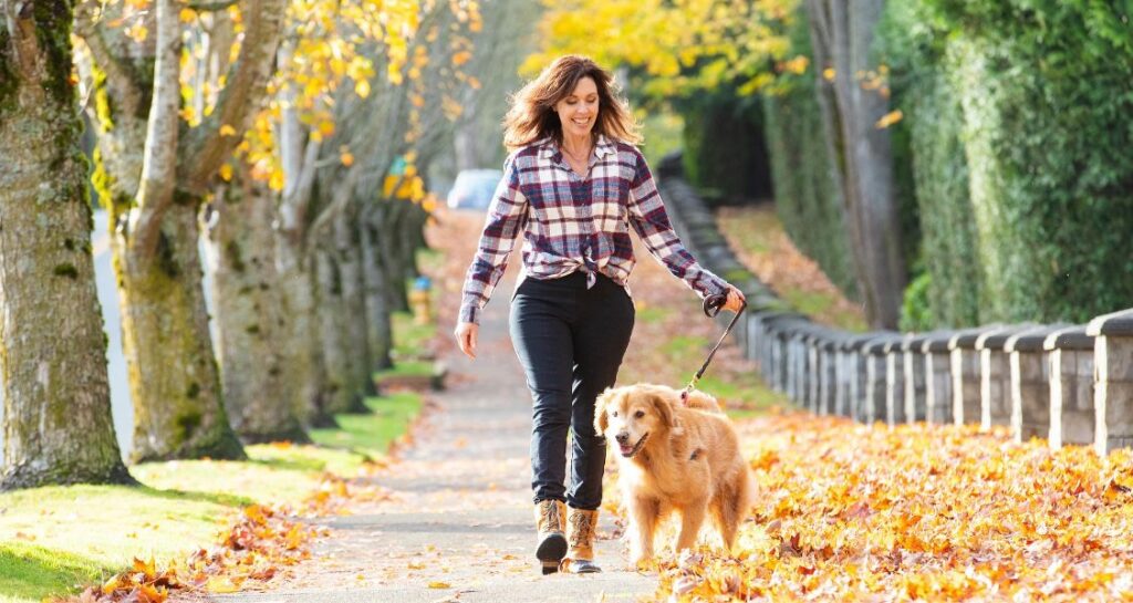 A woman is walking her dog outside during fall