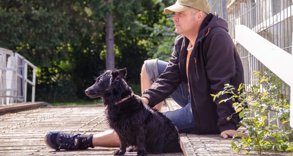 A man is sitting next to his dog outside