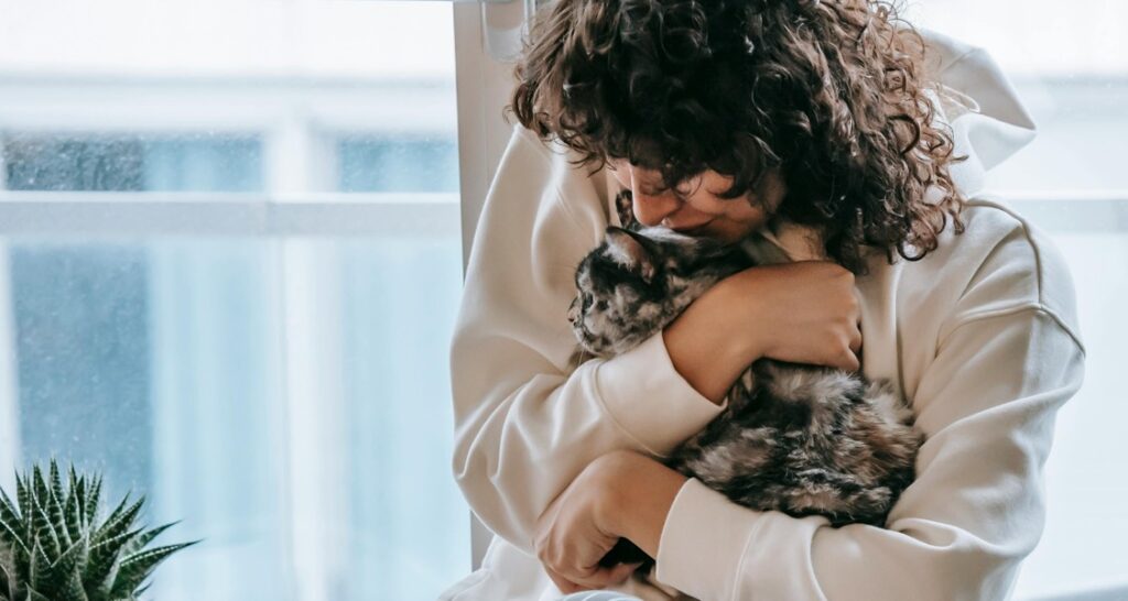 A woman is snuggling a cat in their arms